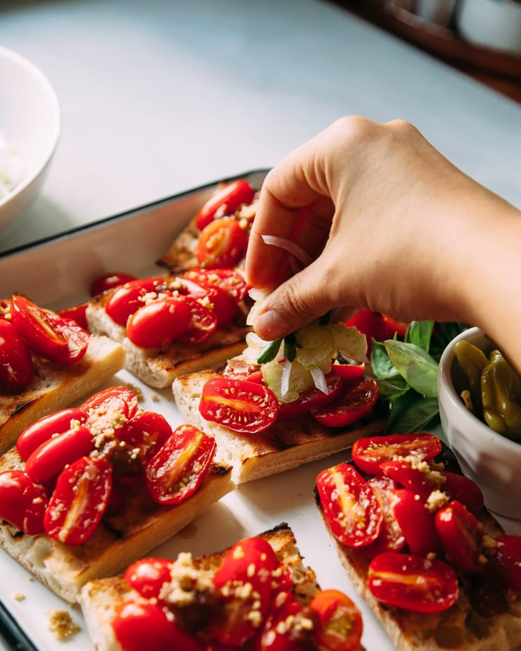 A hand is putting garnishes on top of Bloody Mary bruschetta.