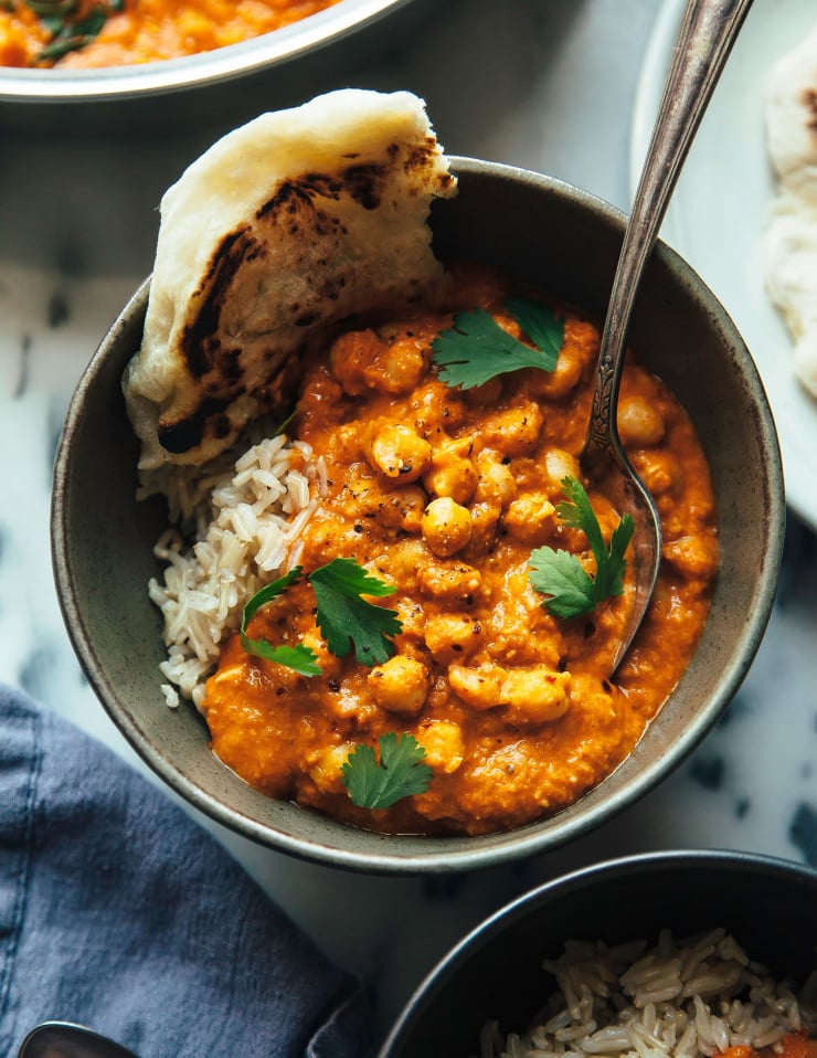 Overhead up close shot of vegan butter chickpeas in an individual bowl with a torn piece of flatbread to the side.