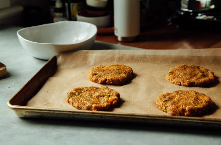 A 3/4 angle shot of formed sweet potato cake patties on a parchment lined baking sheet.