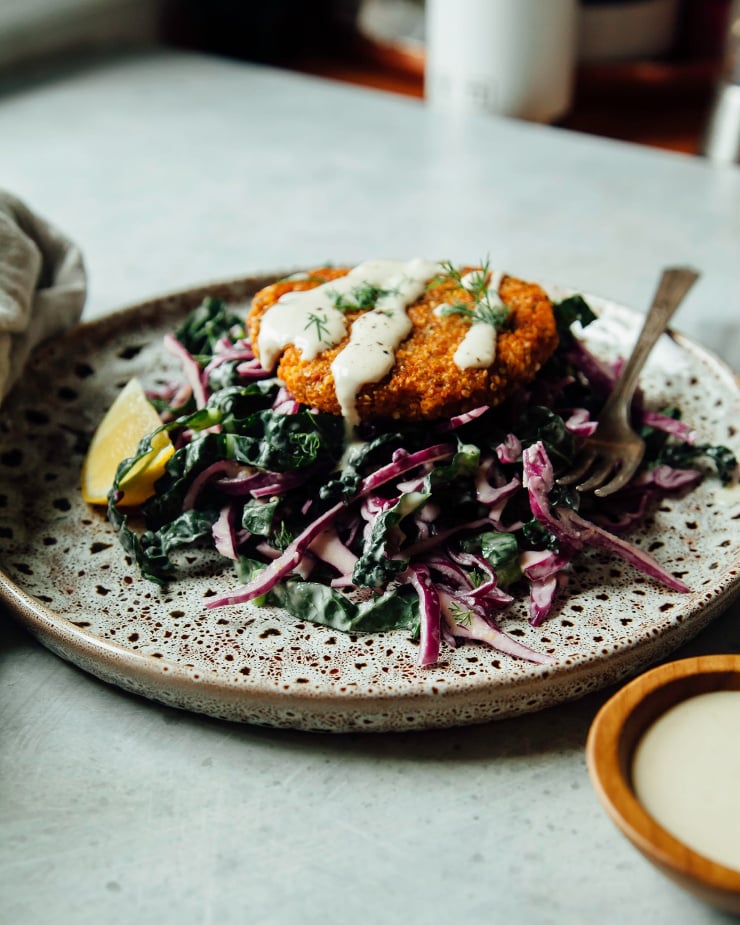 Sweet potato cakes perched on top of a lemony slaw, photo is taken at a side angle with a blue-grey background.