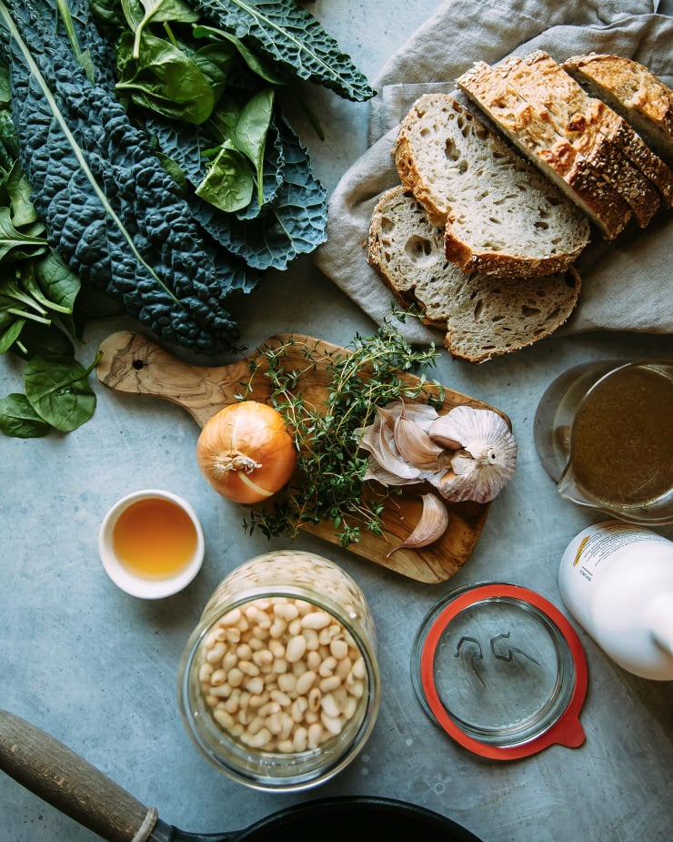 An overhead shot of ingredients for creamy white beans with greens plus some sliced bread.