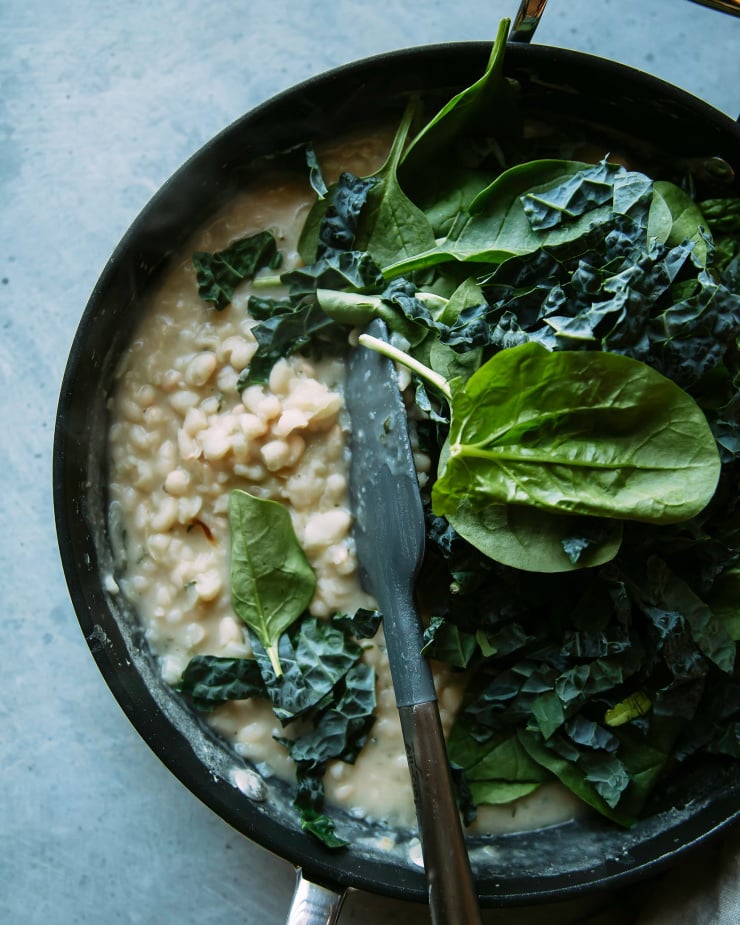 Image shows a spatula stirring greens into lightly puréed white beans.