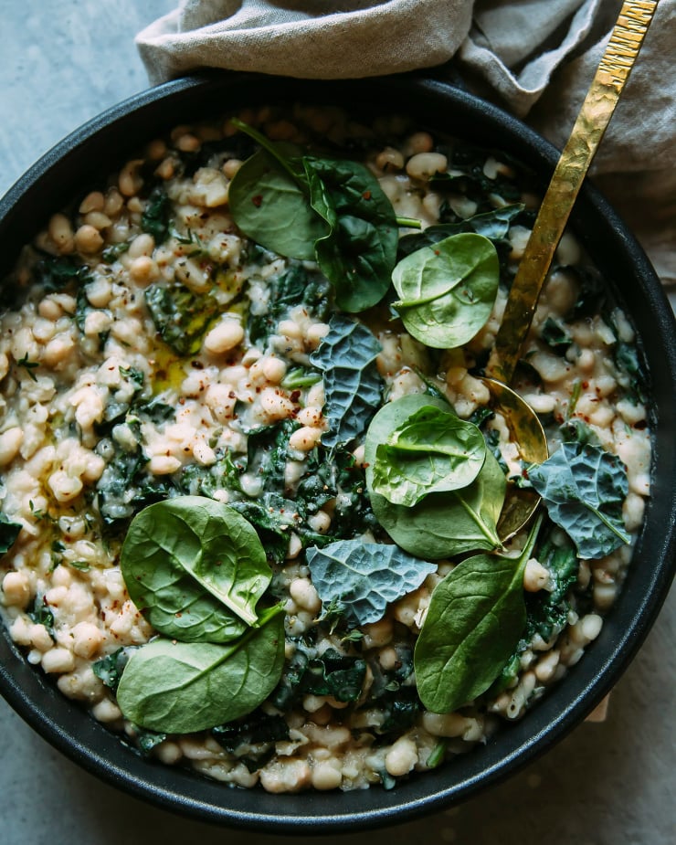 Image shows a creamy white beans and greens mixture in a skillet.