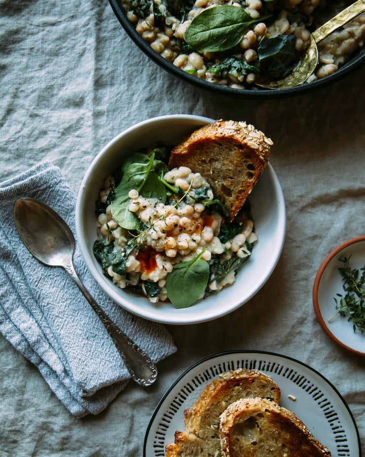 Image shows a single serving of creamy white beans with greens and toasted grainy bread.