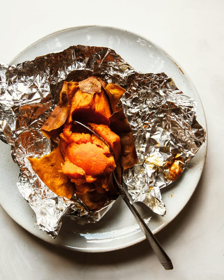 Overhead shot of a baked and opened sweet potato in torn open foil packet on top of a white plate.
