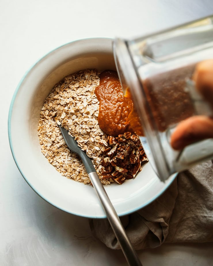 Sweet potato goo is being poured into an enamelware bowl with oats and chopped pecans.