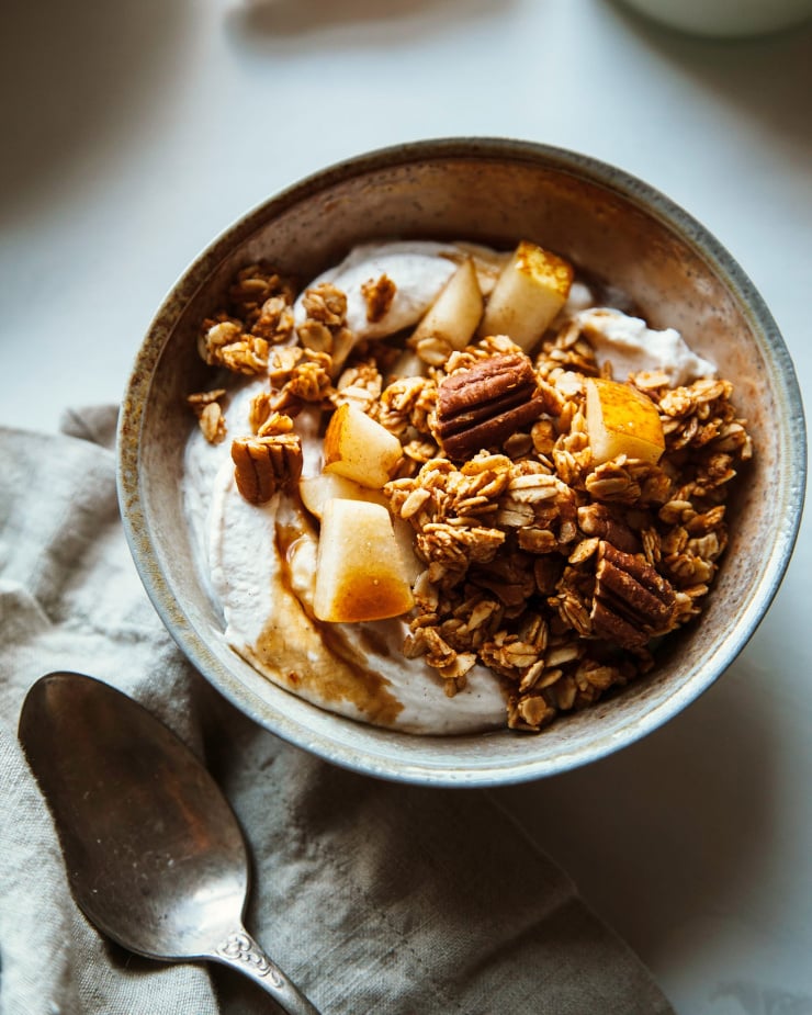 An overhead shot of a bowl of coconut milk yogurt topped with granola and diced pear.