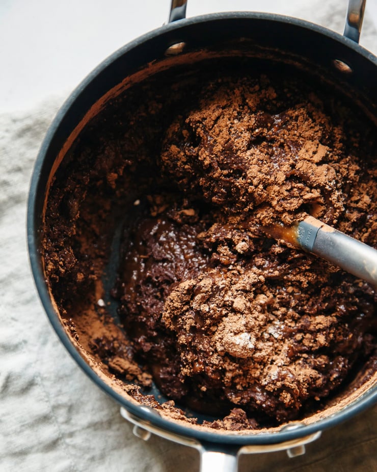 An overhead shot of melted chocolate being mixed with dry ingredients in a medium saucepan.