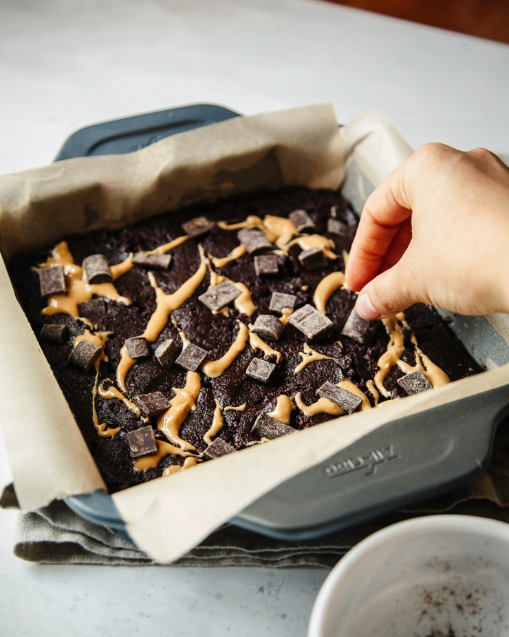 A 3/4 angle shot of a hand placing chocolate chunks on top of a pan of brownies, about to be baked.