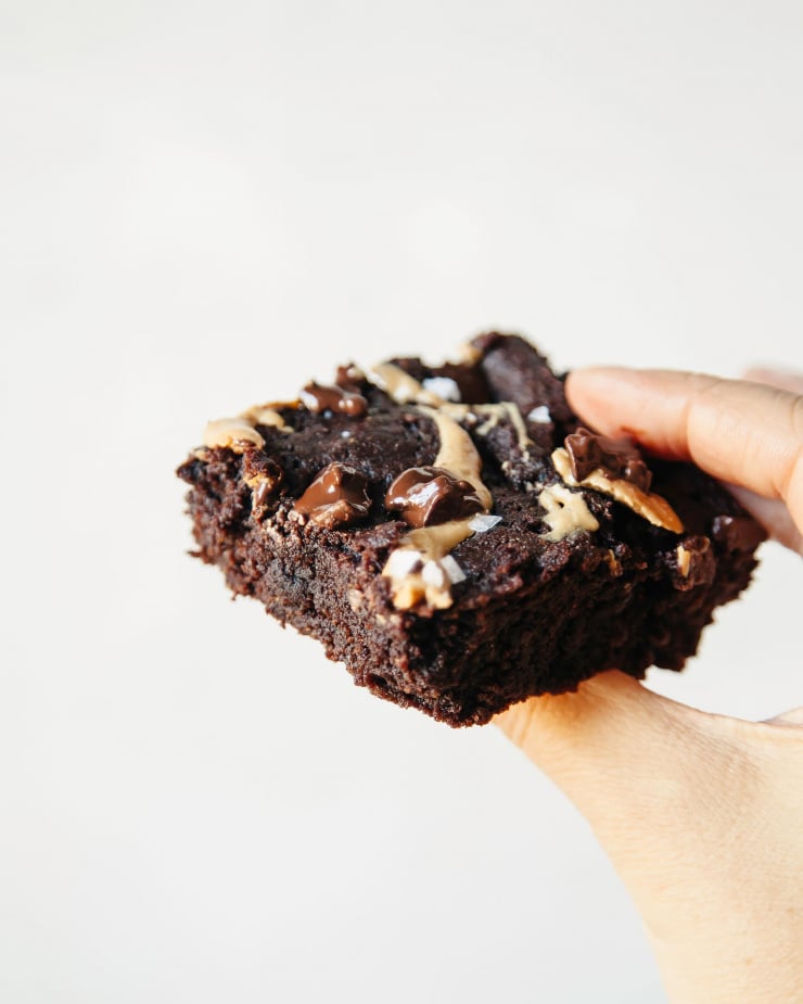 A hand holding a very fudge-y brownie against a bright white background.