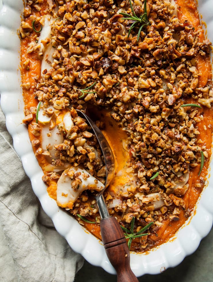 Vegan sweet potato casserole with apples and crunchy rosemary walnuts is shown in a white oval baking dish.
