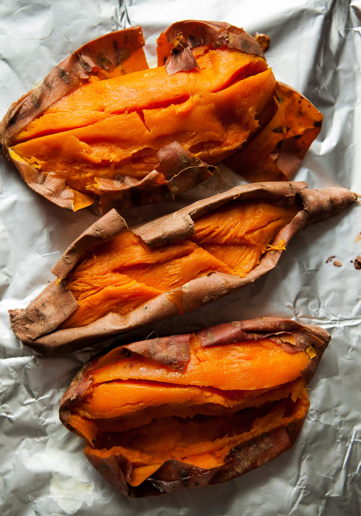 An overhead shot of roasted and split open sweet potatoes on top of foil.