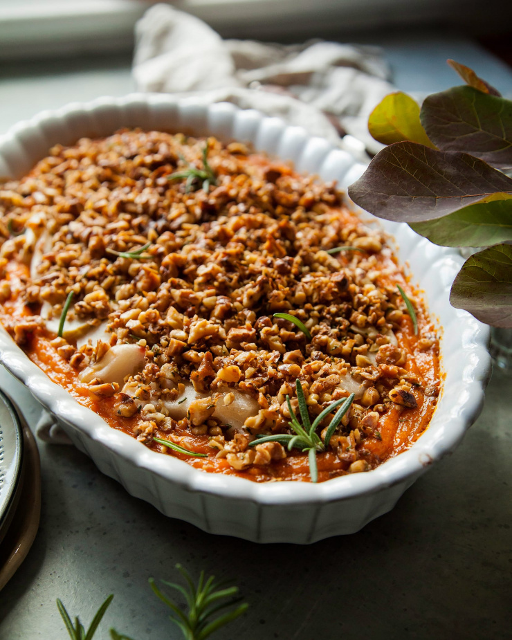A 3/4 angle of a baked vegan sweet potato casserole in an oval-shaped, white baking dish.