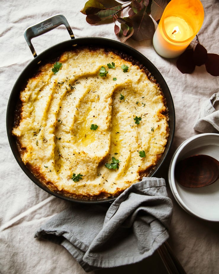 An overhead shot of a vegan French onion shepherd’s pie in a skillet on top of a beige tablecloth.