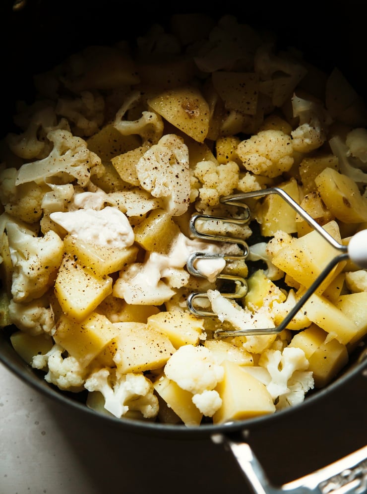 Cooked potatoes and cauliflower are being mashed with vegan butter.