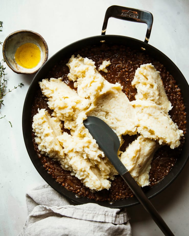 Image shows creamy mashed potatoes and cauliflower being spread on top of a lentil stew mixture.