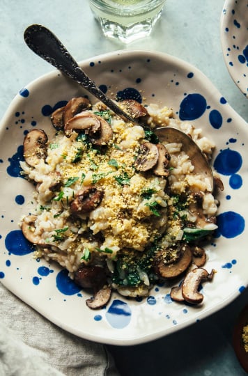 An overhead shot of a serving of mushroom risotto in a blue dot speckled bowl. The risotto also features cooked baby spinach.