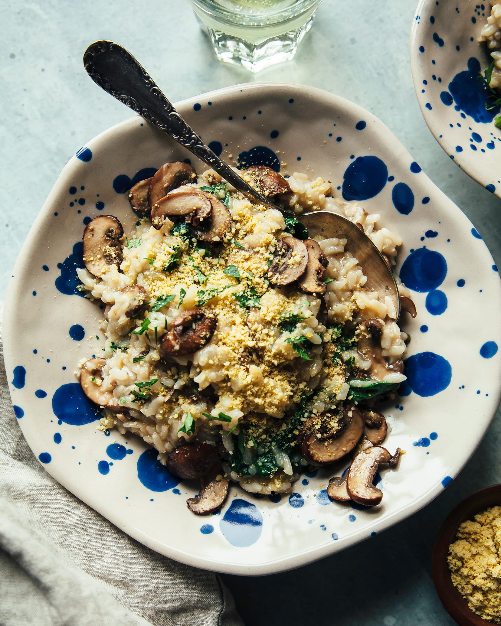 An overhead shot of a serving of mushroom risotto in a blue dot speckled bowl. The risotto also features cooked baby spinach.