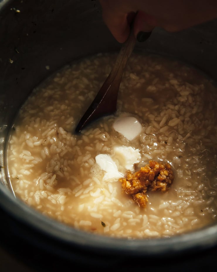 An overhead shot of a hand stirring some risotto.