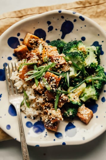An overhead shot of a bowl containing crispy cubes of tofu, broccoli, cooked brown rice and sesame seeds.