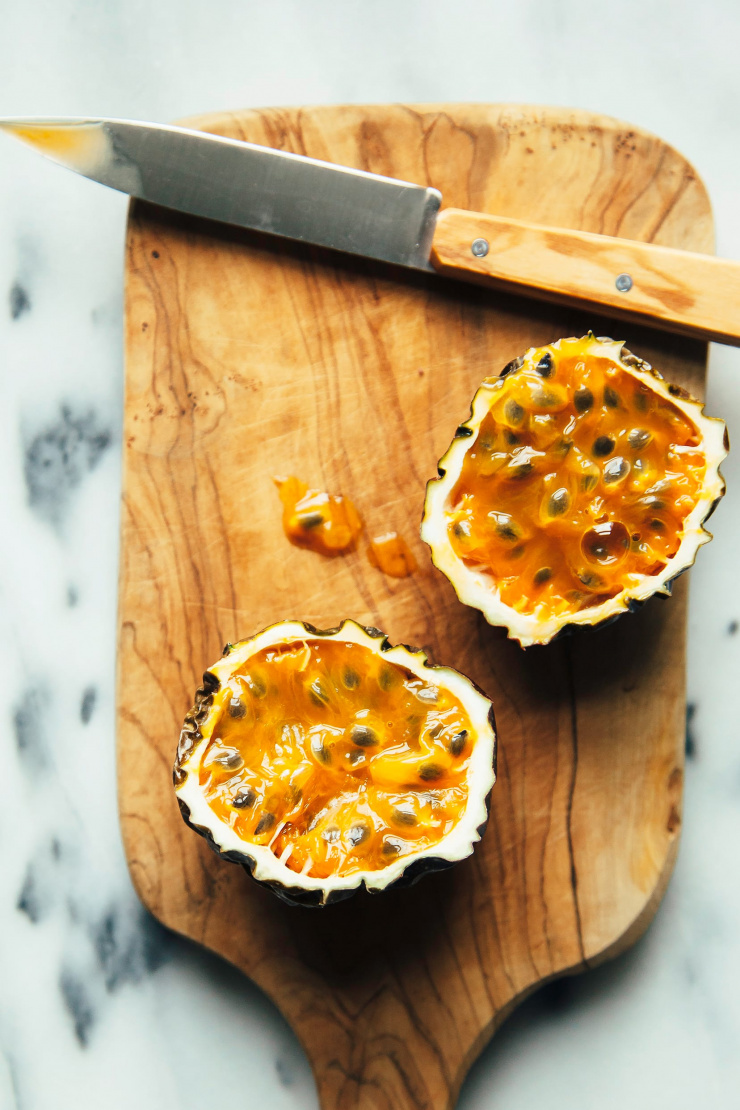 Overhead shot of a cut open passion fruit on a small wooden cutting board.