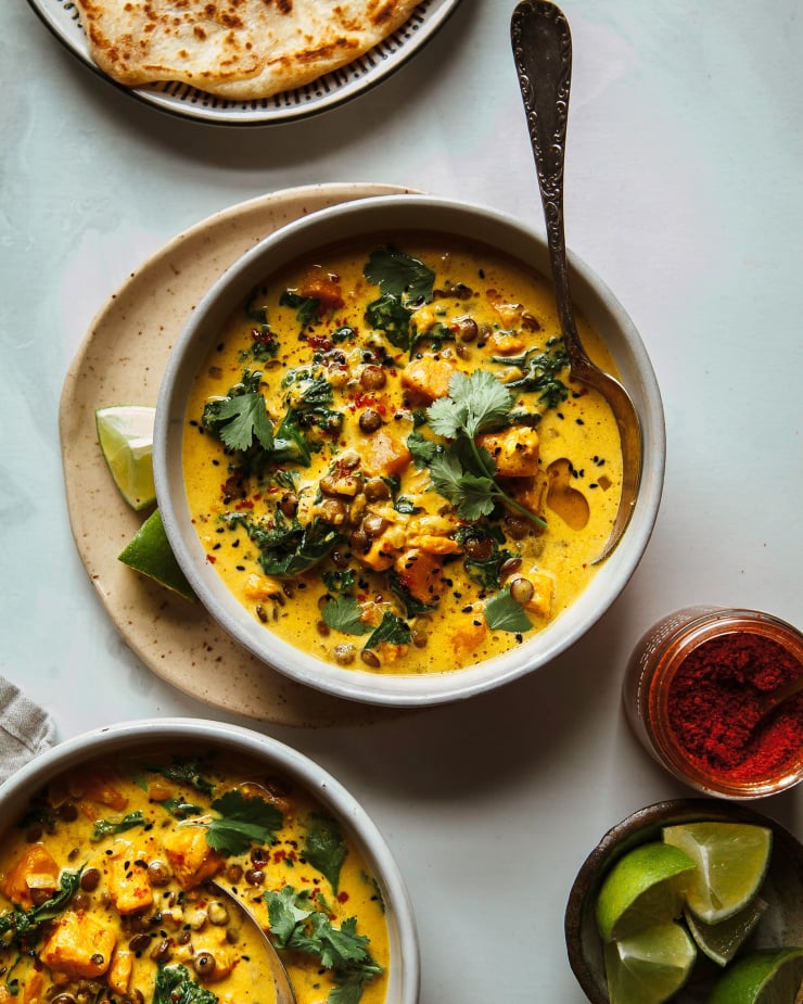 An overhead shot of 2 bowls of sweet potato and coconut milk stew with a few leaves of cilantro on top. The stew is bright orange and creamy