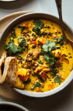 An overhead shot of a sweet potato and coconut milk stew in a bowl. The stew features brown lentils and kale and is topped with cilantro. A folded flatbread is tucked into one corner of the stew.