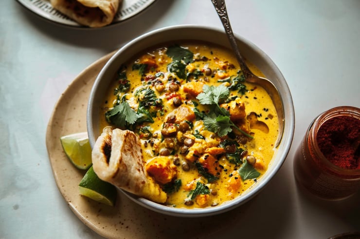 Up close shot of a bowl of sweet potato and coconut milk stew with a few leaves of cilantro on top. The stew is bright orange and creamy