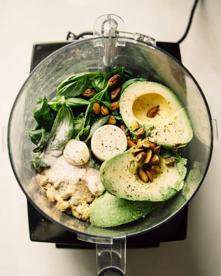 An overhead shot of an open food processor with avocado pesto sauce ingredients.