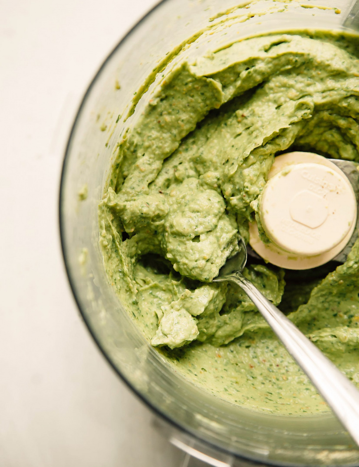 Avocado-based pesto sauce being mixed inside the bowl of a food processor.