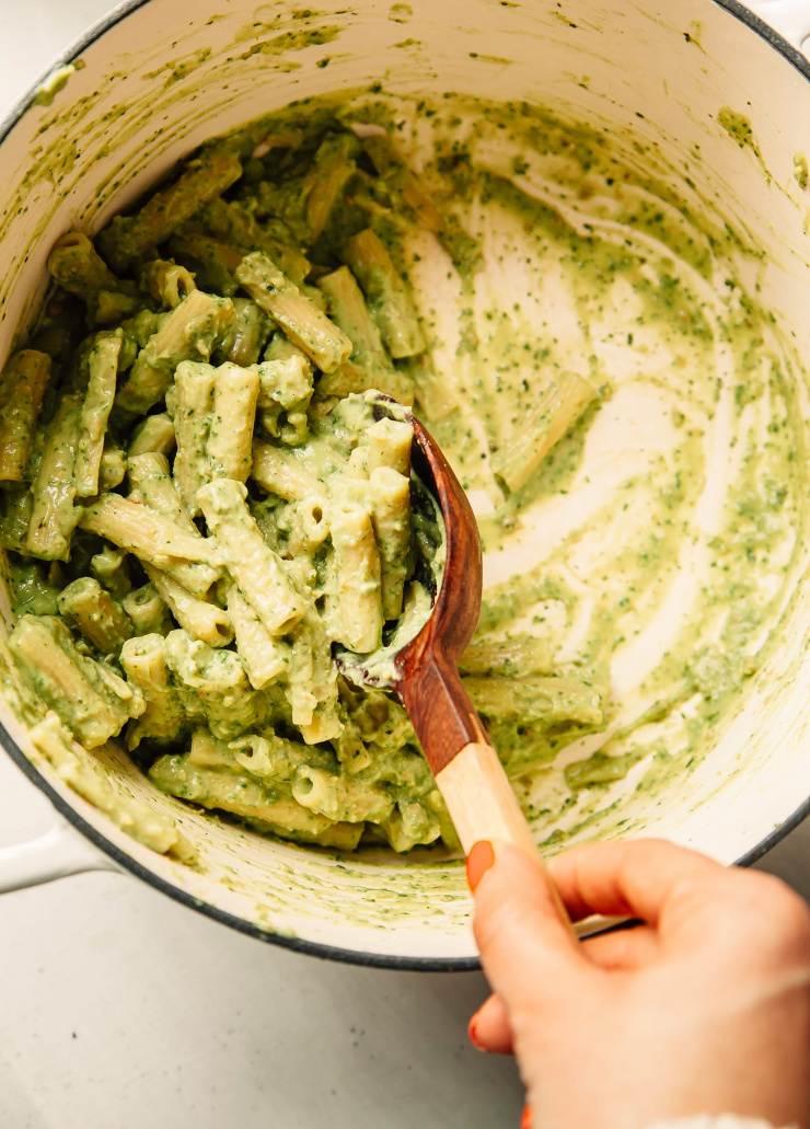 An overhead shot of avocado pesto pasta being stirred in a white pot.