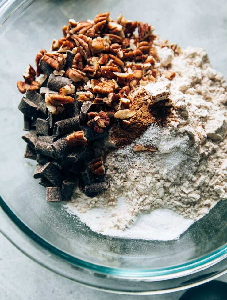 An overhead shot shows dry ingredients plus chocolate chunks and chopped pecans in a mixing bowl.