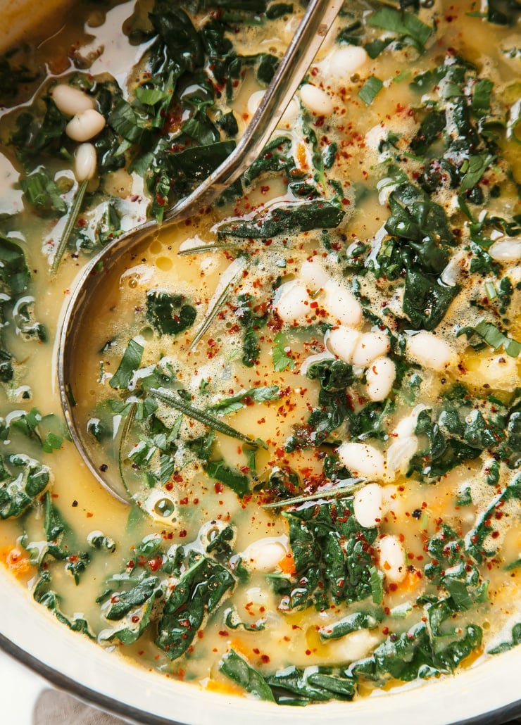 Up close, overhead shot of a creamy white bean soup with rosemary and lemon. The soup is in an off-white pot and there is a ladle in the pot as well.
