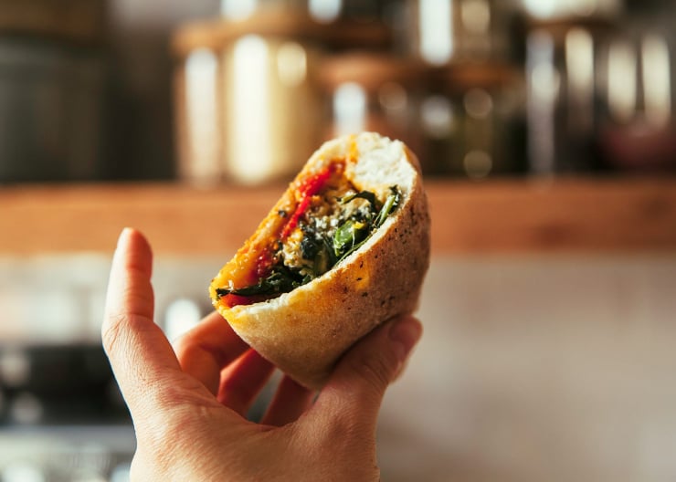 A hand holding half of a vegan sausage calzone.