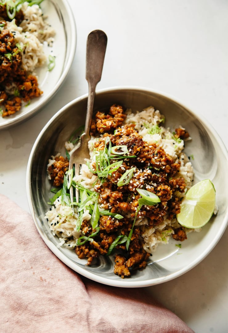 Overhead shot of a bowl of sticky ginger tempeh with coconut rice with a lime wedge alongside.