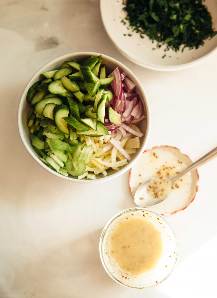 An overhead image of chopped vegetables and herbs in white bowls.