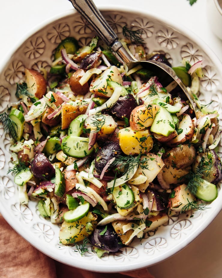 An overhead shot of a vegan potato salad with a vinaigrette dressing and herbs in a white bowl.