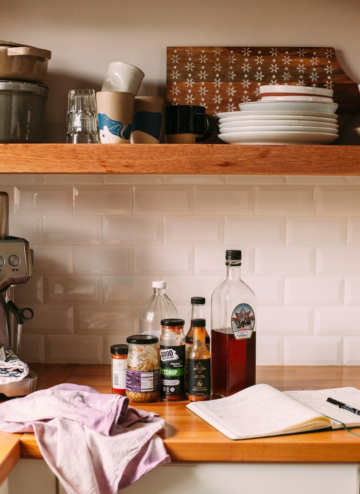 A head-on shot shows a wood counter top against a white tile background. Some pantry ingredients sit on the counter next to a kitchen towel and a notebook.
