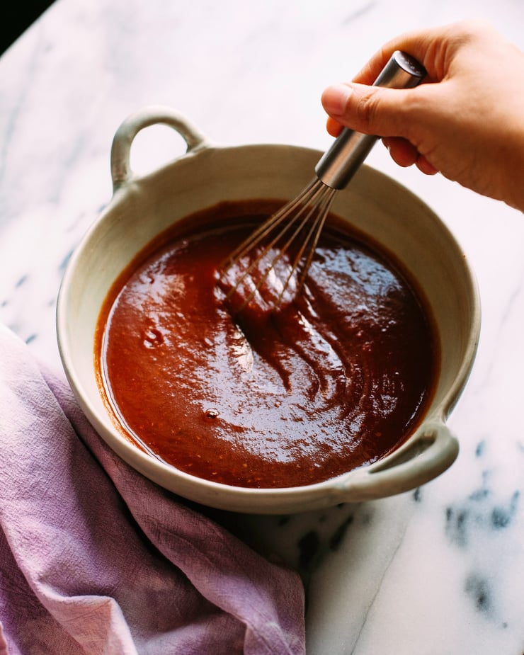 Am overhead shot shows a hand whisking up some maple BBQ sauce in a bowl.