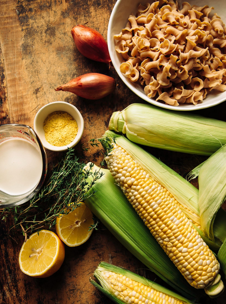 An overhead shot of ingredients for a corn pasta over a weathered wood background.
