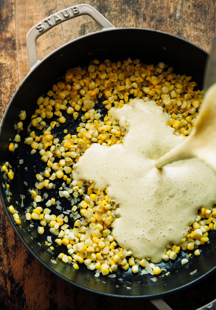 A vegan “cream” is added to a braiser-style pot that has cooked corn inside.