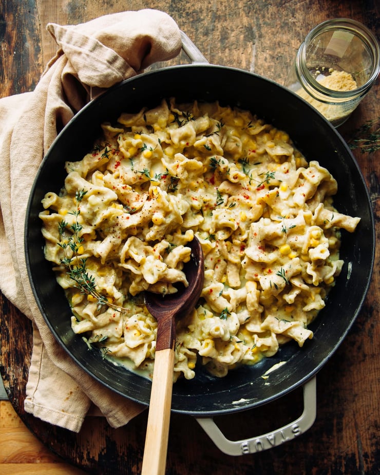 An overhead shot of a creamy, pale yellow pasta in a wide braiser pot over a weathered wood background. There is a pale yellow napkin nearby as well.