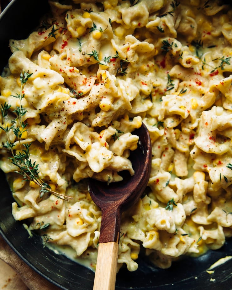 An overhead shot of a creamy corn and lemon pasta in a wide braiser-style pot. There is a wooden spoon sticking out of the pot as well.
