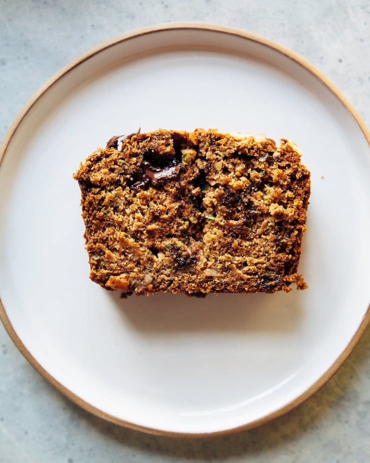 An overhead shot shows a single slice of vegan zucchini bread on a white plate.