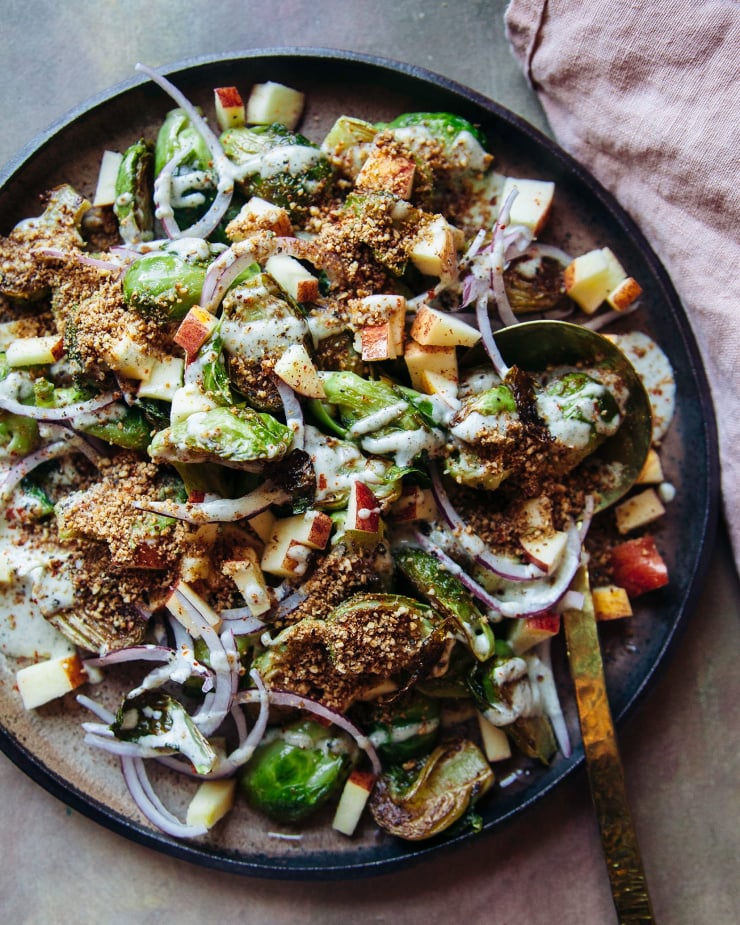 An overhead shot of a roasted Brussels sprout and apple salad with a drizzle of creamy dressing over top.