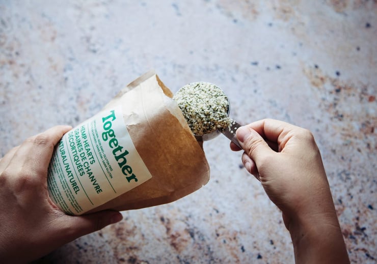 An overhead shot of a hand scooping some hemp seeds from a brown paper bag.
