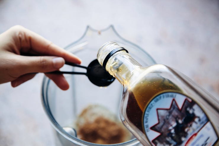 An up close shot of a hand pouring maple syrup into a measuring spoon.