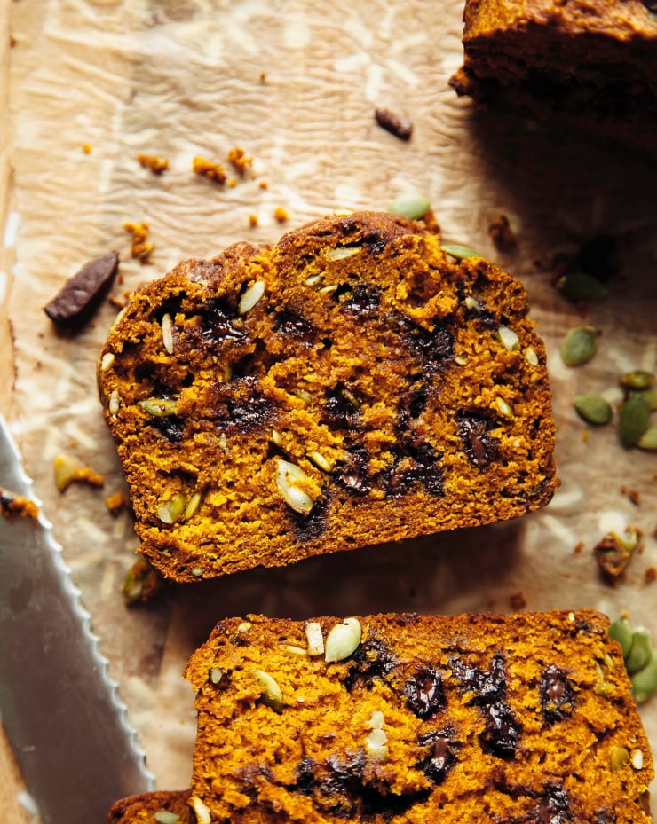 An up close, overhead shot shows a sliced of vegan pumpkin bread that is dotted with chocolate chips and pumpkin seeds