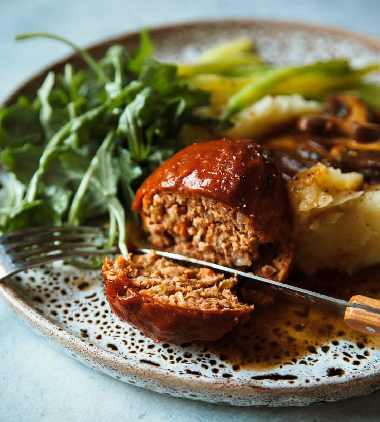 An up close shot of a cut into vegan spicy buffalo meatloaf on a dinner plate with some side dishes. It is taken at side angle.
