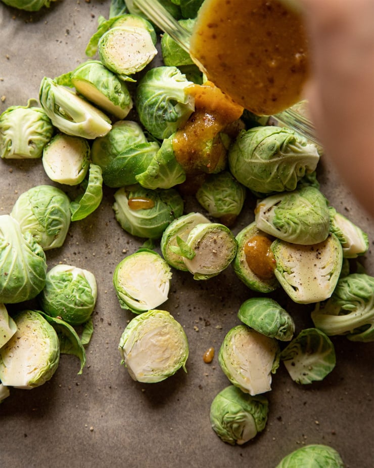 Raw Brussels sprouts being tossed with miso and mustard mixture.